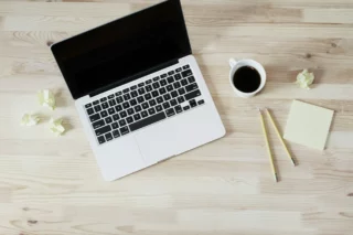 A laptop, pens, paper, and a cup of coffee on a table